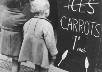 Duas crianças observam um cartaz oferecendo cenouras ao invés de sorvetes durante o grande racionamento de comida na Segunda Guerra Mundial, 1941.